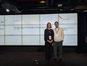 Natasha Banks and Dr. Jake Renzella smile before a screen displaying the words "Google.org Accelerator: Generative AI"